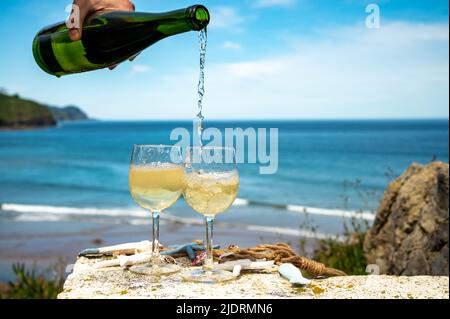 Pouring of txakoli or chacolí slightly sparkling very dry white wine produced in Spanish Basque Country, served outdoor with view on Bay of Biscay, At Stock Photo