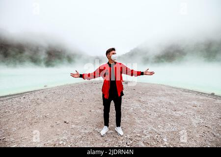 young man in red bomber jacket standing at kawah putih sulfer lake in Bandung Stock Photo