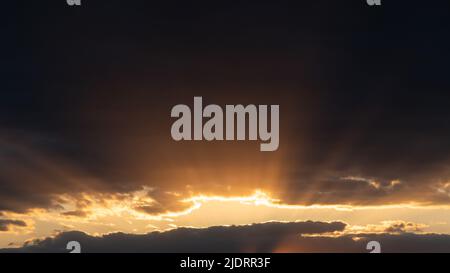 Bright sun rays coming out of gap in dark clouds at sunset, dramatic cloudscape Stock Photo
