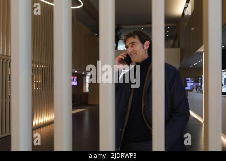 Businessman with smartphone by ear while entering hall of contemporary hotel and calling colleague Stock Photo