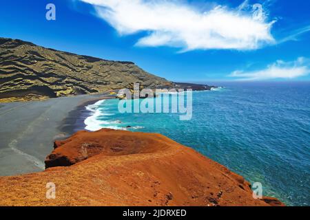 Beautiful secluded lagoon surrounded by impressive rugged weathered cliffs, different colors,red rock,  empty deserted black sand beach - El Golfo, La Stock Photo