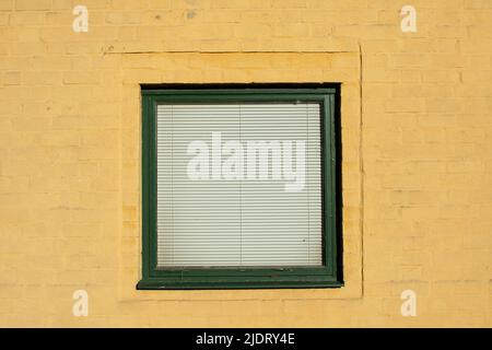 Green window with blinds on yellow plastered old wall Stock Photo
