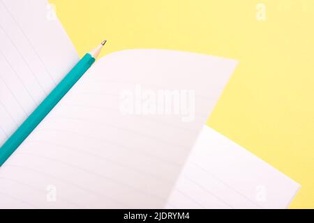 Aqua blue pencil and an open notebook on yellow background. Stock Photo