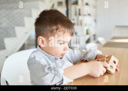 Little boy plays with concentration with a wooden toy for motor skills and dexterity Stock Photo