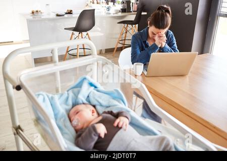Exhausted single mother in home office with sleeping baby in foreground Stock Photo