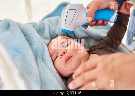 Mother measuring the contactless fever of the baby on the forehead with a clinical thermometer Stock Photo