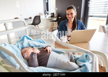 Smiling single mother working from home office and sleeping baby in the foreground Stock Photo