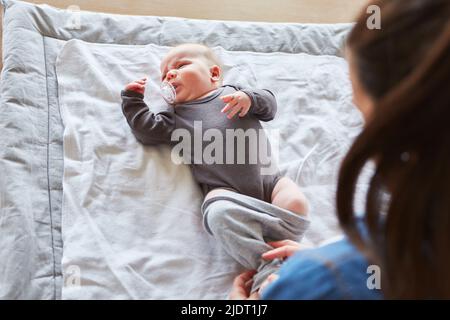 Mother puts a romper suit on her baby after changing diaper Stock Photo