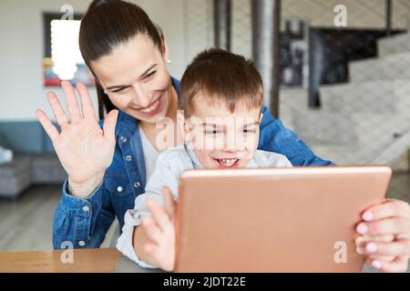 Waving mother and her son video chatting with the grandparents on the PC in the living room Stock Photo