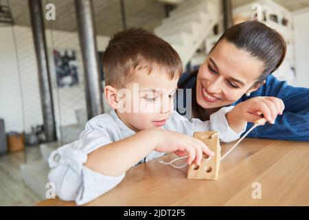 Boy playing with wooden toys for motor skills and concentration under mother's supervision Stock Photo