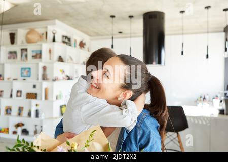 Child hugs his mother and congratulates her on Mother's Day with a bouquet of flowers Stock Photo