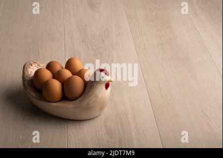 Chicken eggs in a chicken shaped dish on a light wood surface, with negative space for copy Stock Photo