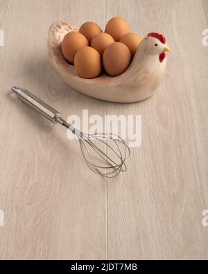 A whisk chicken eggs in a glass bowl and in a chicken shaped dish on a light wood surface, with negative space for copy Stock Photo