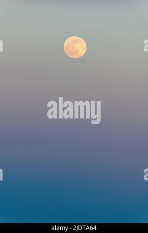 A full moon rising above a blue sea on a perfect evening in Sicily, Italy Stock Photo