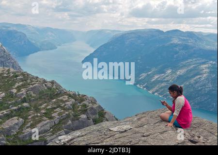 Girl using her smart phone at Preikestolen overlooking Lysefjorden i Forsand county, Rogaland, Norway. Stock Photo