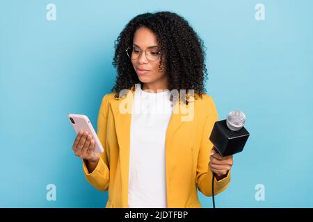 Photo of young black woman look read browse cellphone reporter tv microphone isolated over blue color background Stock Photo