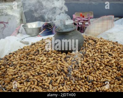 Heap of roasting raw peanuts, Smoke coming out of pot with peanuts below. peanut also known as the groundnut, goober, pindar or monkey nut. Stock Photo