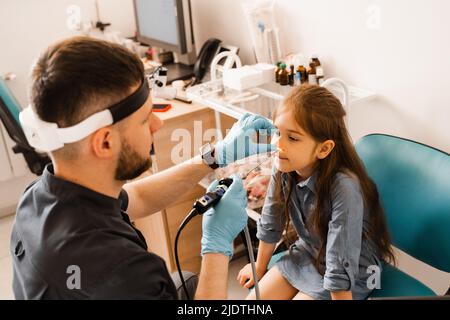 Nose endoscopy of child. Rhinoscopy procedure with rhinoscope. ENT doctor otolaryngologist with headlight treat nose kid patient Stock Photo