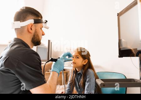 Nose endoscopy of child. Rhinoscopy procedure with rhinoscope. ENT doctor otolaryngologist with headlight treat nose kid patient Stock Photo