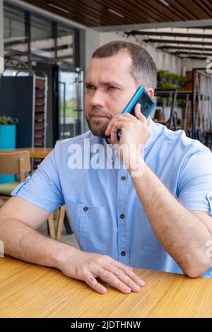 A middle-aged Arab man with a beard is talking on the phone in an outdoor cafe. Smiling middle aged businessman freelancer using mobile phone Stock Photo