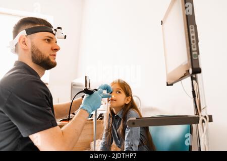 Nose endoscopy of child. Rhinoscopy procedure with rhinoscope. ENT doctor otolaryngologist with headlight treat nose kid patient Stock Photo