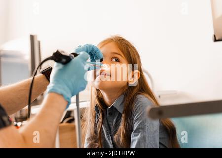 Nose endoscopy of child. Rhinoscopy procedure with rhinoscope. ENT doctor otolaryngologist with headlight treat nose kid patient Stock Photo