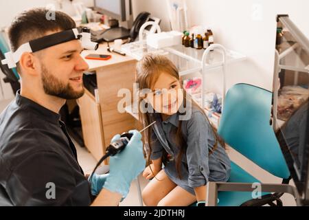 Nose endoscopy of child. Rhinoscopy procedure with rhinoscope. ENT doctor otolaryngologist with headlight treat nose kid patient Stock Photo