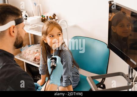 Nose endoscopy of child. Rhinoscopy procedure with rhinoscope. ENT doctor otolaryngologist with headlight treat nose kid patient Stock Photo