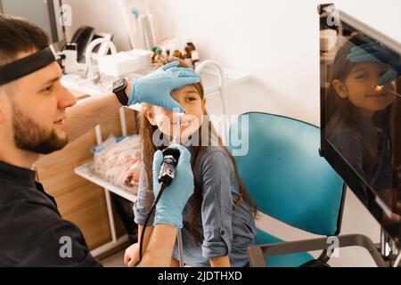 Nose endoscopy of child. Rhinoscopy procedure with rhinoscope. ENT doctor otolaryngologist with headlight treat nose kid patient Stock Photo