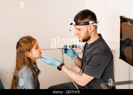 Nose endoscopy of child. Rhinoscopy procedure with rhinoscope. ENT doctor otolaryngologist with headlight treat nose kid patient Stock Photo