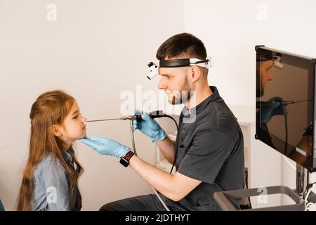 Nose endoscopy of child. Rhinoscopy procedure with rhinoscope. ENT doctor otolaryngologist with headlight treat nose kid patient Stock Photo