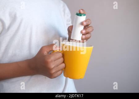 young man putting artificial sweetener in tea, Stock Photo
