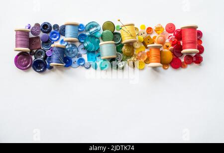 A lot of buttons and reels with colorful threads, laid out on a white background in the colors of the rainbow. Copy space. Stock Photo