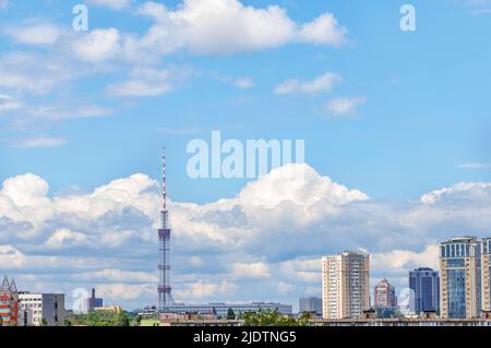 The sharp spire of a television tower rises above white and gray clouds in an urban summer landscape at noon. Copy space. Stock Photo