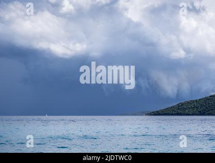 Turquoise sea against dark grey clouds with boat on the horizon at Mikros Gialos on the Ionian island of Lefkada Stock Photo