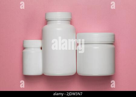 Three empty plastic jars with lids on a pink background Stock Photo