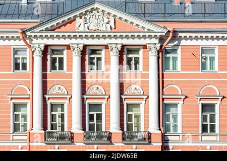 Facade of the building with pink walls with bas-relief, windows, balconies and white columns. From the series windows of St. Petersburg. Stock Photo