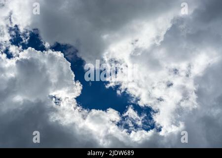 Fragment of a bright blue sky showing through gray fluffy clouds, for use as an abstract background and textures. Stock Photo