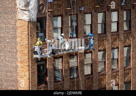 Construction workers high above an urban street in New York City in a suspended basket, Midtown Manhattan, USA  2022 Stock Photo