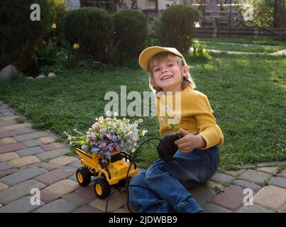 bouquet of flowers in back of toy dump truck near cute smiling boy 6 years old. Business concept - congratulations, builder's holiday, motorist's day, Stock Photo