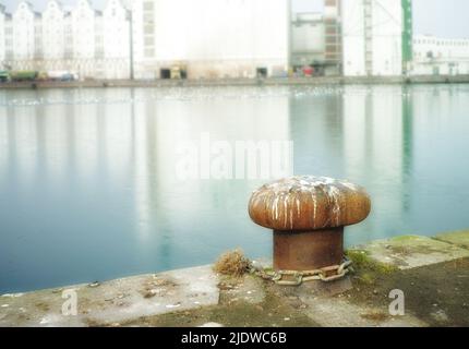 Rusty mooring bollard cast iron at pier shore.A bollard port by a harbour. Sky and water background copyspace. Securing anchor point to prevent Stock Photo