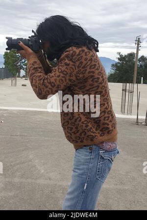 Side view of a long haired young man photographer taking photo with DSLR camera while standing outside Stock Photo