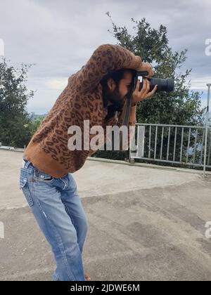 Side view of a attractive long haired and bearded young man photographer taking photo with DSLR camera while standing outside Stock Photo