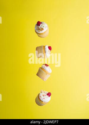Appetizing little muffins with whipped cream and fresh raspberries on a bright yellow background in frozen flight. There are no people in the photo. B Stock Photo