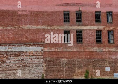 An old warehouse exterior wall of crumbling brick and windows without glass. Stock Photo