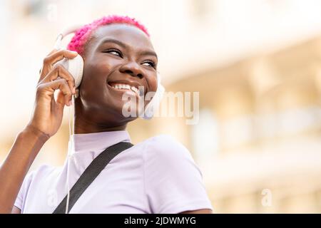Smiling afro woman using headphones on the street Stock Photo