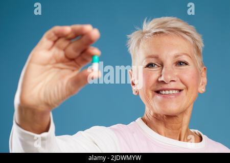 Close-up of satisfied female medical scientist standing against blue background and holding capsule while discovering new drug Stock Photo