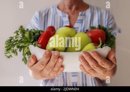 Close-up, an elderly woman holds a bowl of vegetables in her hands. Stock Photo