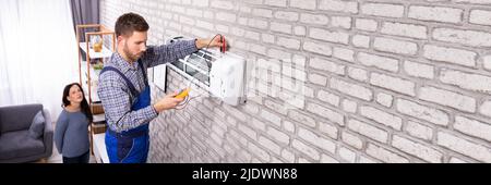 Young Woman Looking At Technician Examining Air Conditioner With Digital Multimeter Stock Photo