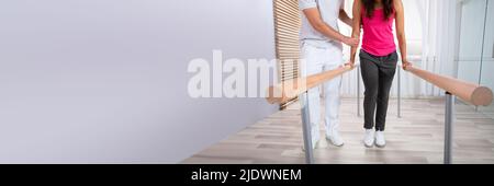 Female Patient Being Assisted By Physical Therapist While Walking With The Support Of Handrails Stock Photo